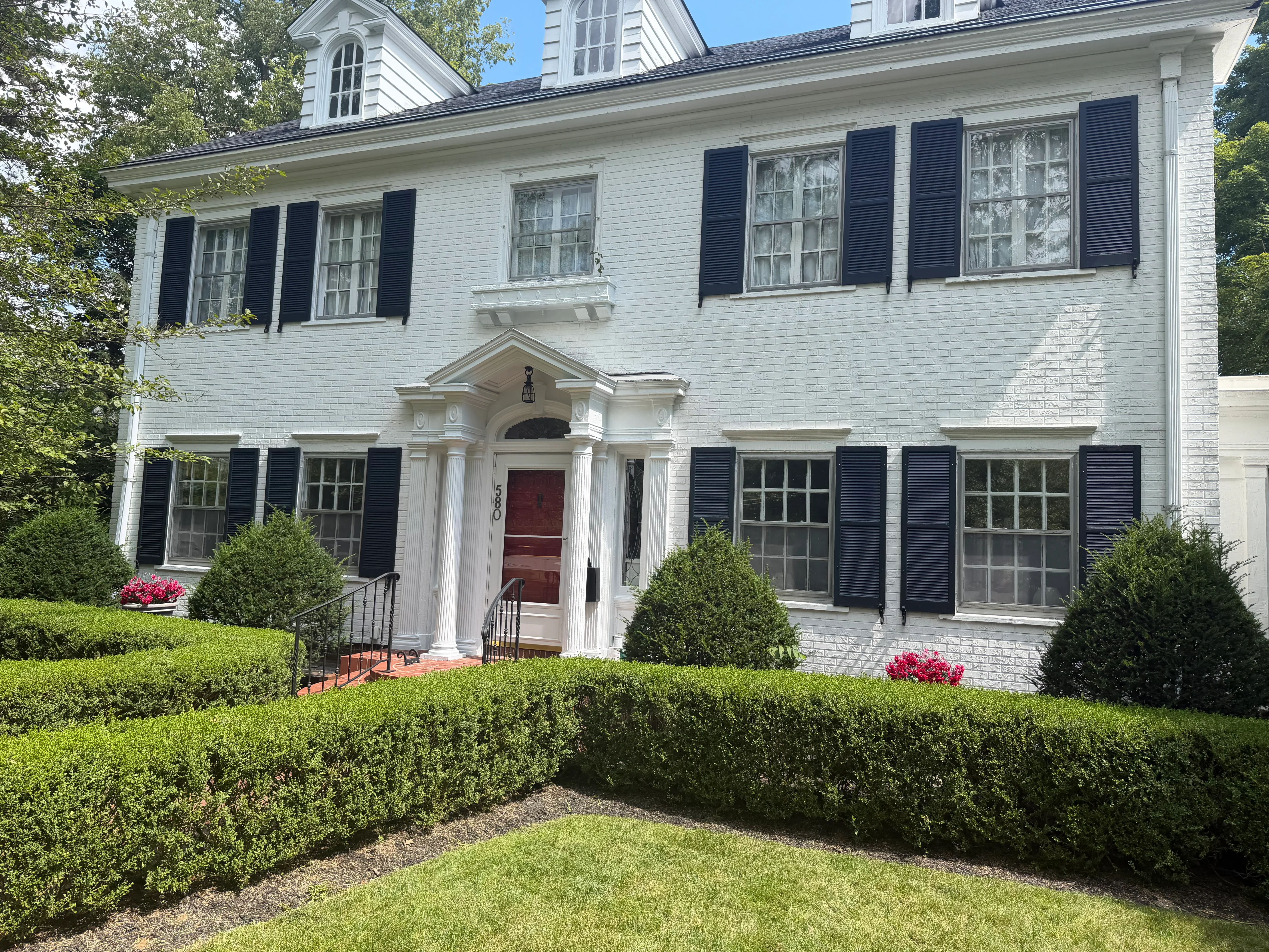 White brick colonial home with black shutters, painted trim, and burgundy door