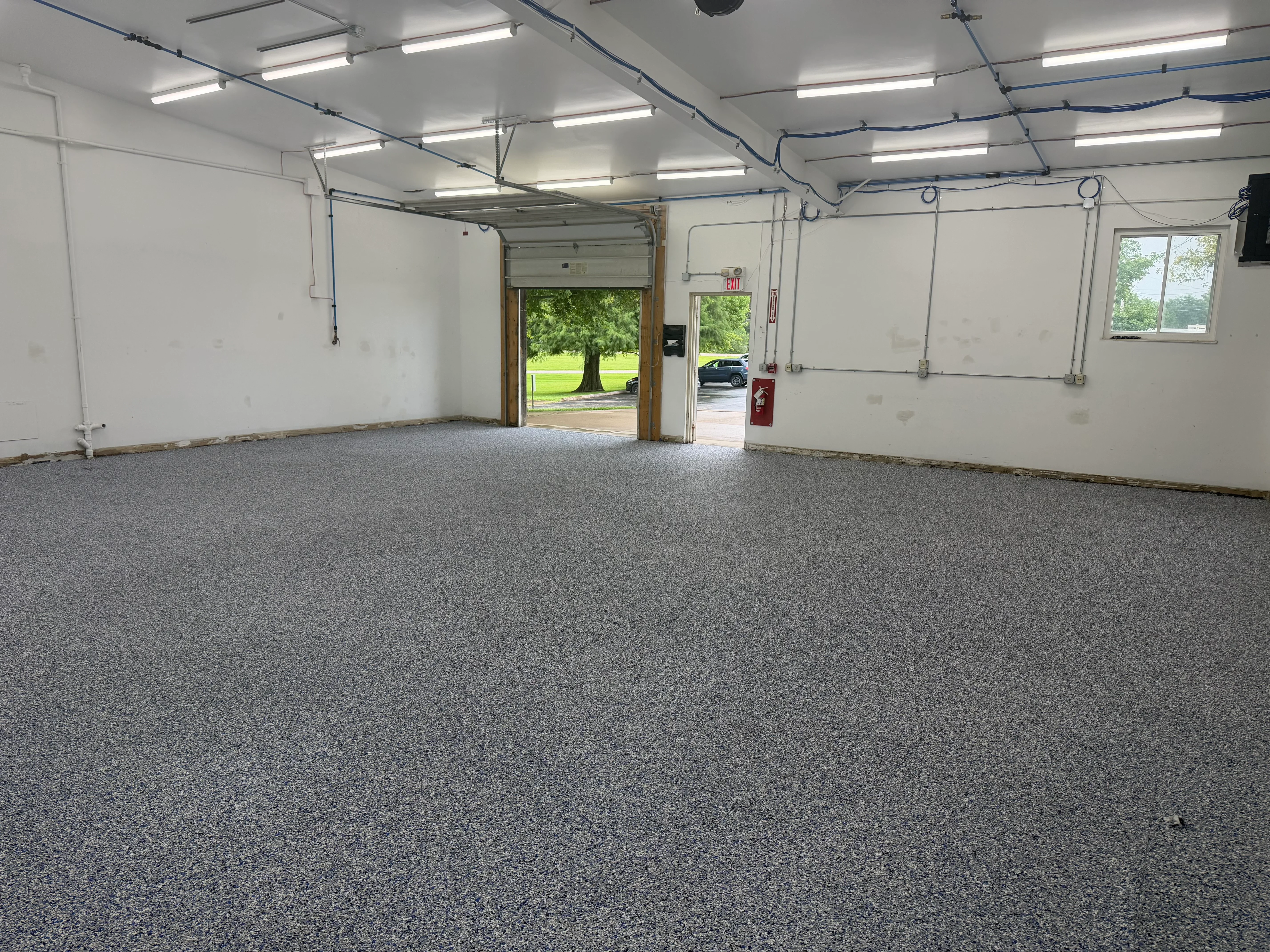 Gray epoxy garage floor with white walls, overhead lighting, and garage door entrance